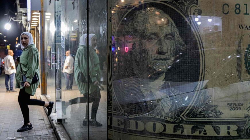 A woman walks out of a currency exchange shop displaying a giant US dollar banknote in the Zamalek district of Egypt's capital Cairo on August 24, 2022. - Depleted foreign currency reserves are casting a shadow on Egyptian streets, with the government moving to dim lights to free up energy for export. More natural gas exports means more hard currency, a dire need as experts say a new loan from the International Monetary Fund (IMF) and an adjacent currency liberalisation is inevitable. (Photo by Khaled DESOU