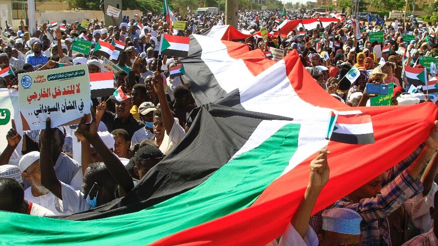 Sudanese protesters deploy a giant national flag, as they march outside the UN headquarters in Khartoum on December 3
