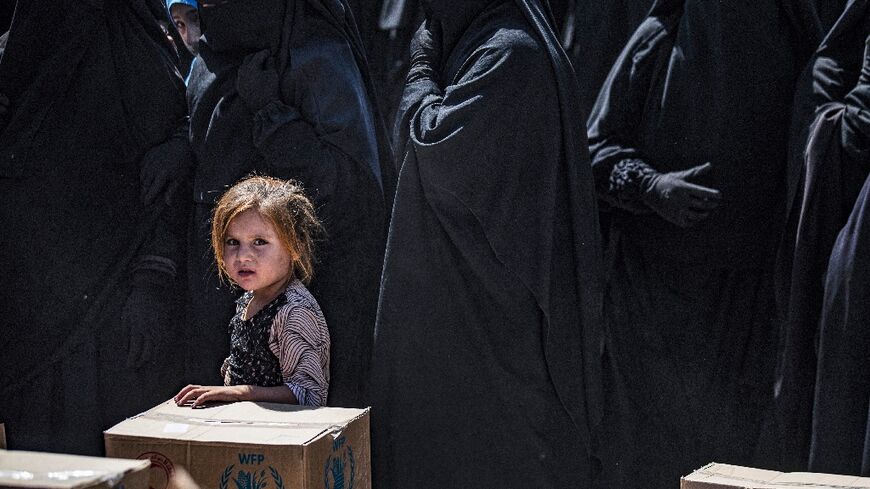 Women and a child queue to receive humanitarian aid packages at the Kurdish-run Al-Hol camp in Syria
