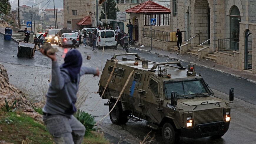 A Palestinian hurls a stone at an Israeli military vehicle during a dawn incursion by the army into the West Bank city of Nablus