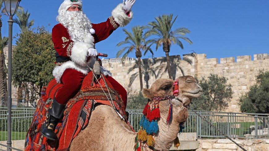 Issa Kassissieh, dressed as Santa Claus, poses for a picture as he rides a camel at Jaffa Gate in Jerusalem's Old City