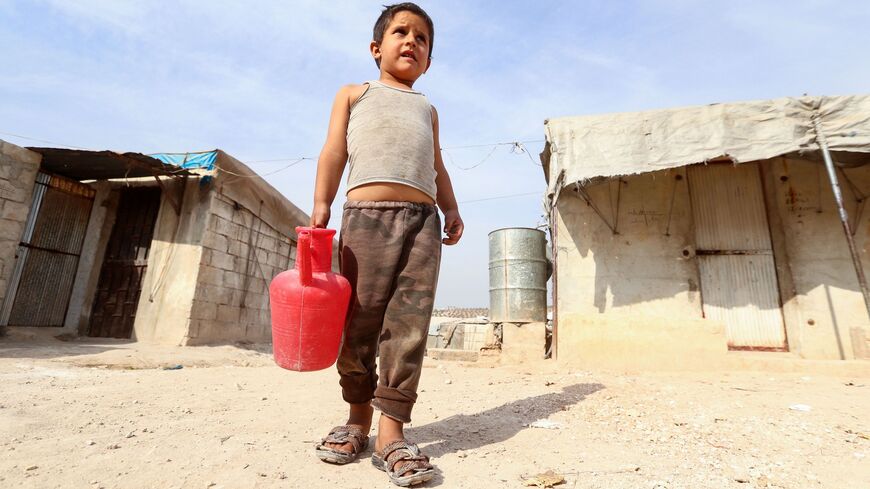A displaced Syrian child carries a jug of water.