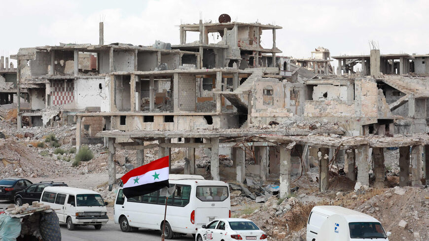 A picture taken during a tour organized by the Syrian Ministry of Information shows a Syrian national flag and cars in the district of Daraa al-Balad, Daraa, Syria, Sept. 12, 2021.