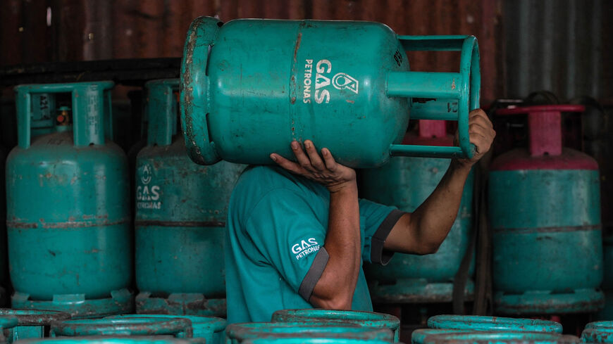 A worker carries an empty Petronas gas cylinder on his shoulder at a shop in Ampang, in the suburbs of Kuala Lumpur, Malaysia, Feb. 29, 2016.
