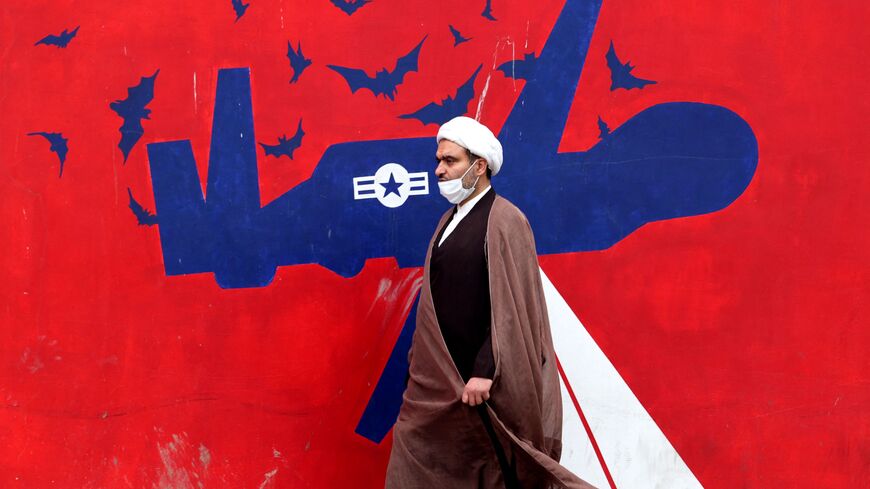 An Iranian cleric walks past an anti-US mural on a wall of the former United States embassy in the capital Tehran, on March 12, 2022. - Iran said that US attempts to seize its tankers and oil cargo had failed to stop exports that are subject to sanctions imposed by its arch foe.  (Photo by ATTA KENARE/AFP via Getty Images)