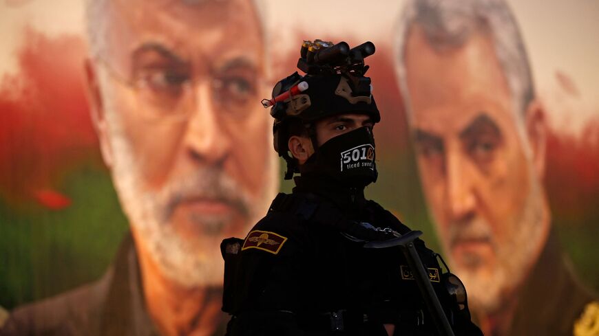 A member of Iraq's Hashed al-Shaabi stands guard in front of a banner depicting slain Iraqi commander Abu Mahdi al-Muhandis (L) and Iranian Revolutionary Guards commander Qasem Soleimani, near Baghdad's International Airport on January 2, 2023. (Photo by AHMAD AL-RUBAYE/AFP via Getty Images)