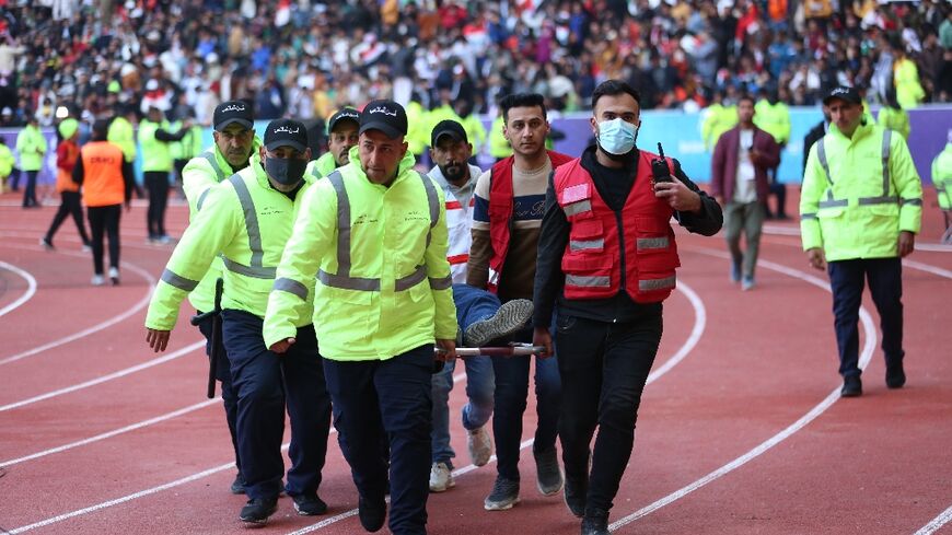 Iraqi security personnel carry an injured football fan into an emergency area at the Basra International Stadium following the stampede
