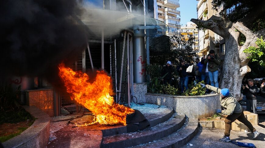 A protester throws a brick at a bank after setting fire to tyres during a demonstration in Beirut