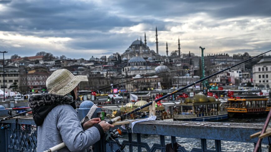 People fish from the Galata bridge, near Suleymaniye mosque (backround) in the Eminonu district of Istanbul, on January 10, 2023.  (Photo by OZAN KOSE/AFP via Getty Images)