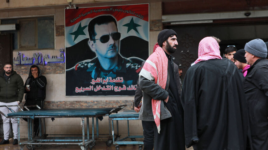 Syrians gather near a poster of President Bashar al-Assad hanging outside the emergency section of a hospital in Hama, on February 6, 2023, following a deadly earthquake. - The Syrian government urged the international community to come to its aid after more than 850 people died in the country following a 7.8-magnitude earthquake in neighbouring Turkey.(Photo by LOUAI BESHARA/AFP via Getty Images)