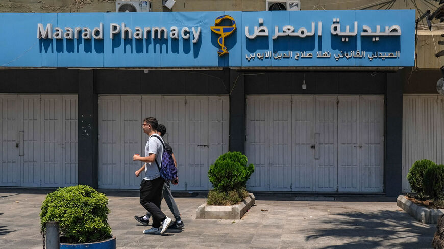 People pass in front of the shuttered door of a pharmacy during a nationwide strike of pharmacies to protest against a severe shortage of medicine, Tripoli, Lebanon, July 9, 2021.