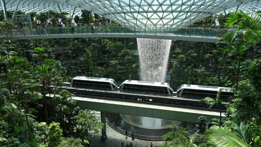 People take picture from a observation bridge of Rain Vortex as a train passes at Jewel Changi airport in Singapore on December 7, 2022. (Photo by Roslan RAHMAN / AFP) (Photo by ROSLAN RAHMAN/AFP via Getty Images)