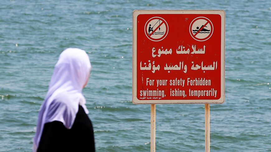 A Kuwaiti woman walks past a warning sign at a beach in Kuwait City, following an oil spill off the coast, Kuwait, Aug. 21, 2017.