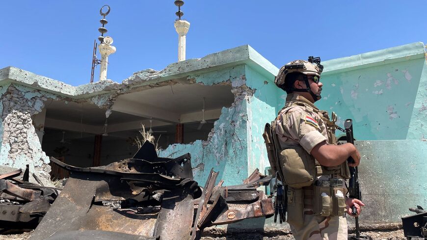 A member of the Iraqi security forces stands by a destroyed vehicle that was carrying rockets amdist sacks of flour, in the district of al-Baghdadi in al-Anbar province on July 8, 2021. - Fourteen rockets were fired on July 7 at an air base hosting American troops in the western province of Anbar, causing minor injuries to two personnel, the coalition said. The rockets "landed on the base & perimeter" of the Ain al-Assad base, the coalition spokesman tweeted, adding that local homes and a mosque were also d