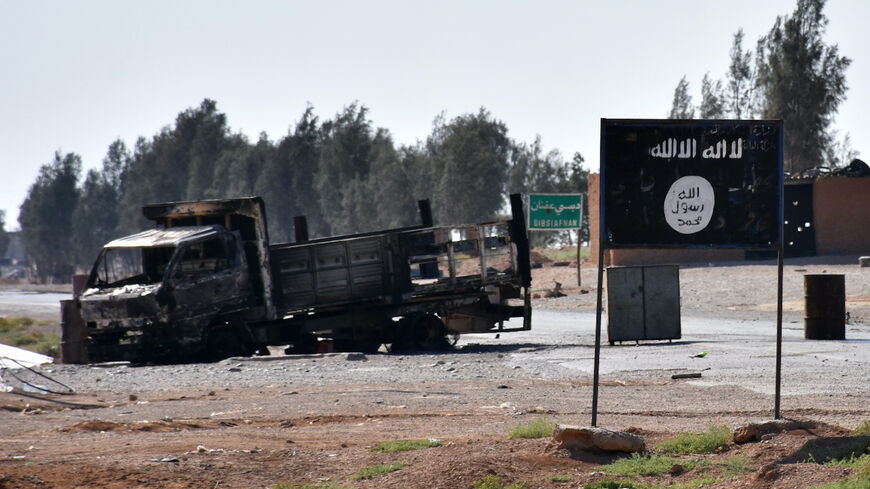 A general view shows a burnt out vehicle next to a banner bearing the Islamic State group's flag in the village of Dibsiafnan on the western outskirts of the Islamist's Syrian bastion of Raqa, after Syrian pro-government forces entered the area on June 11, 2017. / AFP PHOTO / George OURFALIAN (Photo credit should read GEORGE OURFALIAN/AFP via Getty Images)