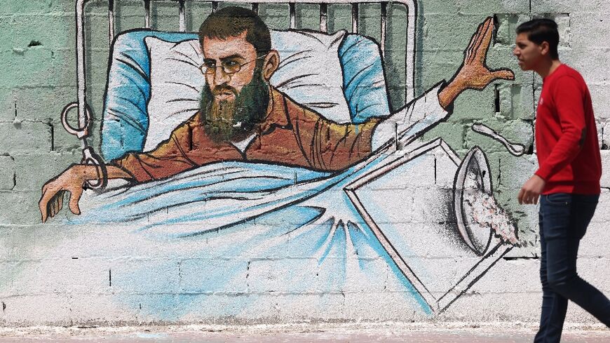 A Palestinian walks past a wall-painting in Gaza of leading Islamic Jihad figure Khader Adnan, who has been on hunger strike for more than 80 days in protest at his detention without charge in an Israeli prison