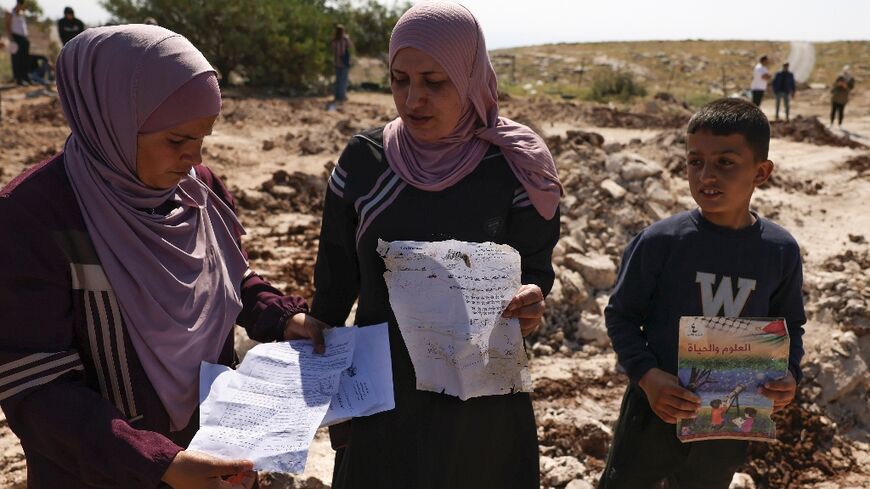 Palestinians pick up papers and books from the site of a school that was demolished by Israeli authorities who said it was built without permission in Jabbet al-Dhib village, east of Bethlehem in the occupied West Bank