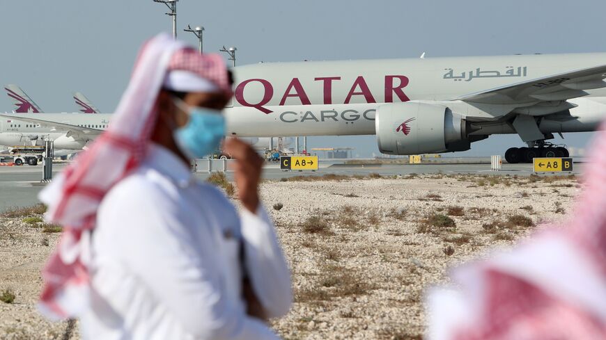 Qatari men walk next to a Qatar Airways cargo airplane on the tarmac of Hamad International Airport near the capital Doha, as the first commercial flight to Saudi Arabia in three and a half years following a Gulf diplomatic thaw prepares to take off, on January 11, 2021. (Photo by KARIM JAAFAR / AFP) (Photo by KARIM JAAFAR/AFP via Getty Images)