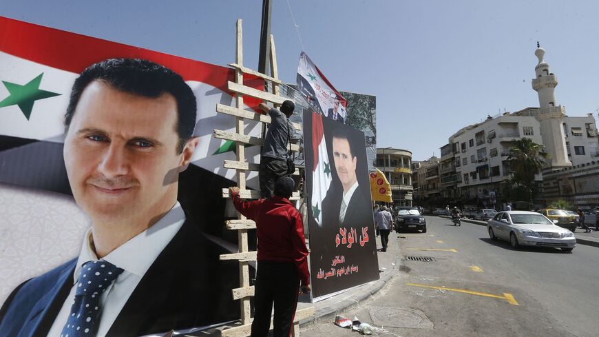 Men hang the national flag next to posters of President Bashar al-Assad, a candidate for the Presidential election, in the Syrian capital Damascus on May 17, 2021. 