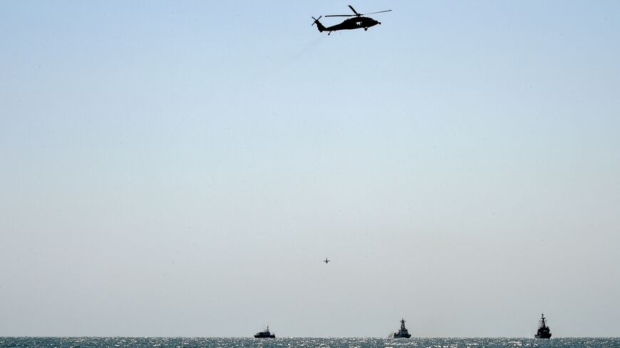  A US Navy Martin UAV drone hovers mid-air beneath a US Navy SH-60S Seahawk helicopter, while Bahraini Coast Guard ship Deraa 13 (L), US Coast Guard cutter Maui (C), and Royal Bahrain Naval Force (RBNF) Abdulrahman Al Fadhel (R) operate on Gulf waters during joint naval exercise between US 5th Fleet Command and Bahraini forces, on October 26, 2021. - The US and Bahrain navies conducted a joint exercise at sea, launching a series of drills integrating unmanned systems into regional maritime operations. (Phot
