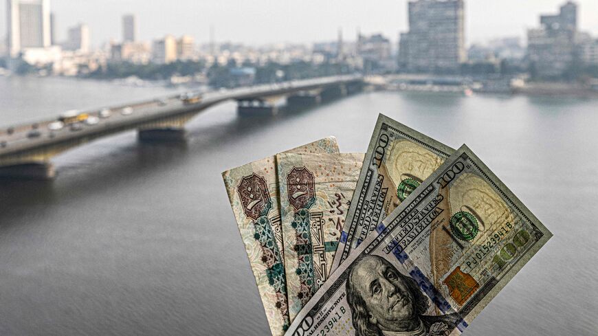 Two pairs of US hundred dollar and Egyptian hundred pound notes are held before a window showing the skyline of Egypt's capital Cairo and the Nile river on January 16, 2023. - With Egypt's economy in crisis, the currency in freefall and inflation skyrocketing, the poor have been hit hard but the middle class is also teetering on the brink. The Egyptian pound has lost half its value against the dollar since March, following a devaluation demanded as part of a $3 billion International Monetary Fund loan agree
