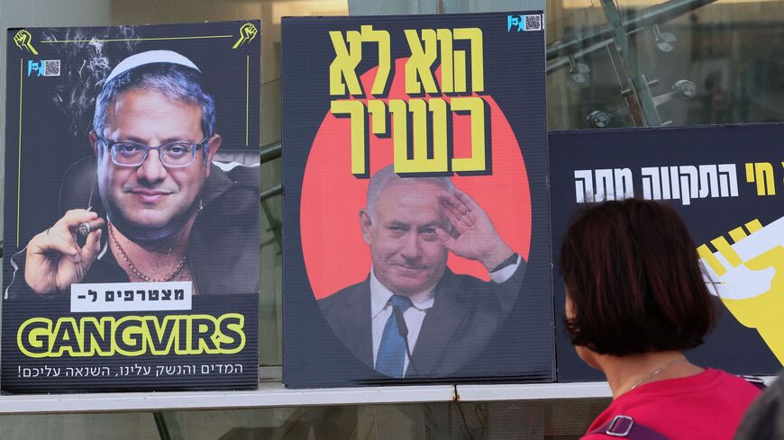 A demonstrator looks at placards depicting Israeli Prime Minister Benjamin Netanyahu and National Security Minister Itamar Ben-Gvir (L).