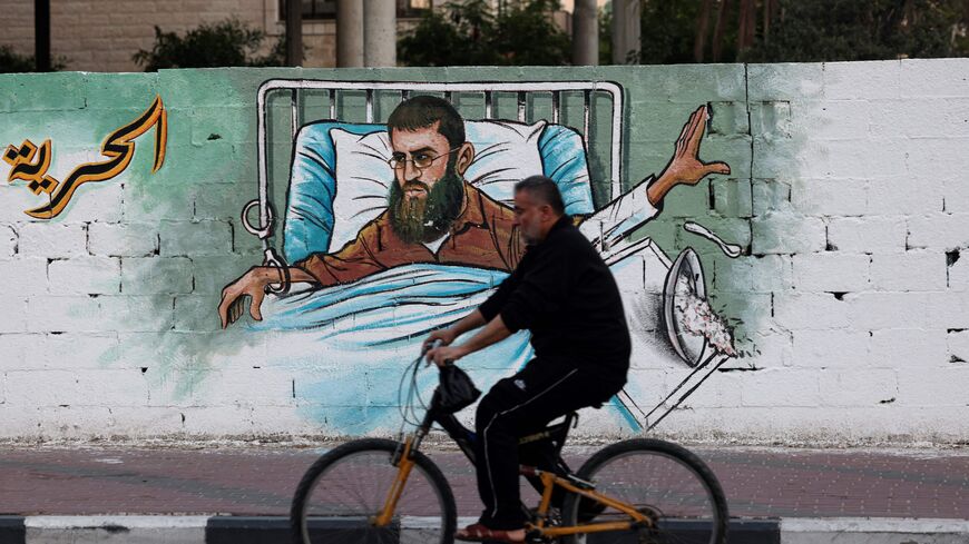 A Palestinian man rides his bike past a mural depicting Khader Adnan, a Palestinian hunger striker and top figure in the Islamic Jihad group in the occupied West Bank, in Gaza City on May 2,2023. - Khader Adnan began a hunger strike on February 5, 23, died on May 2, 2023, the prison service said in a statement, adding that he was "affiliated with the Islamic Jihad". (Photo by MOHAMMED ABED / AFP) (Photo by MOHAMMED ABED/AFP via Getty Images)