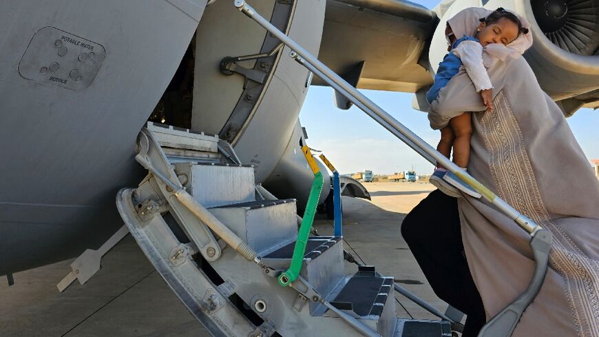 An evacuee holding a sleeping toddler boards an Abu Dhabi-bound plane at Port Sudan airport