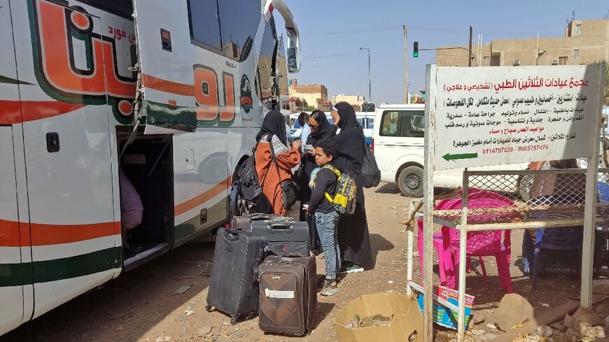 People wait with their luggage at a bus stop in southern Khartoum, preparing to join the exodus