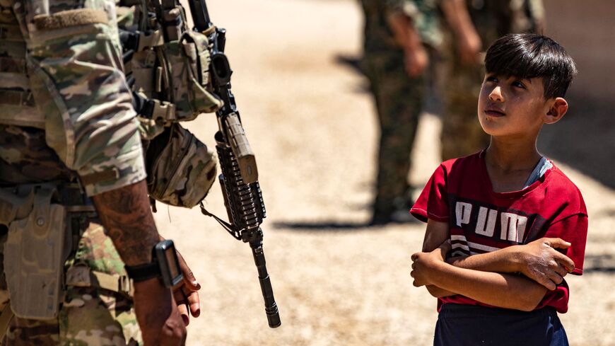 A child stares at a US soldiers patrolling a village in the countryside of the Kurdish-majority city of Qamishli in Syria's northeastern Hasakeh province, near the Turkish border, on July 23, 2022. (Photo by Delil SOULEIMAN / AFP) (Photo by DELIL SOULEIMAN/AFP via Getty Images)