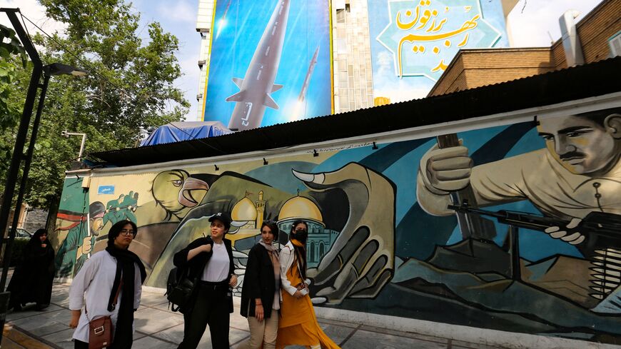 Women walk along a mural painting behind which appears a giant billboard bearing a picture of the 'Fattah' hypersonic missile, in Tehran on July 7, 2023. Iran's Revolutionary Guards unveiled an intermediate range ballistic missile on June 6 capable of travelling at hypersonic speeds of up to 15 times the speed of sound, state television reported. (Photo by ATTA KENARE / AFP) (Photo by ATTA KENARE/AFP via Getty Images)