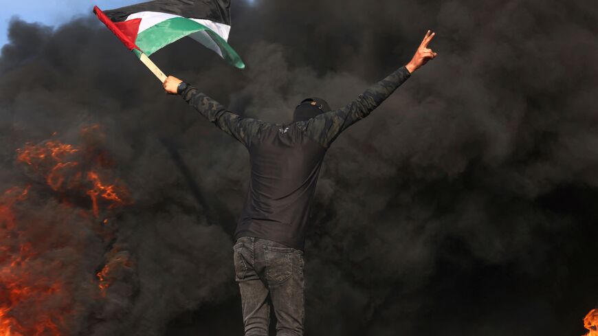 A Palestinian youth flashes the victory sign as tyre smoke billows during a protest by the border fence with Israel east of Gaza city on June 19, 2023 following an Israeli raid in the West Bank. Israeli forces in the occupied West Bank killed five Palestinians including a militant on June 19, in a raid that saw eight Israeli security personnel wounded and rare helicopter fire. (Photo by Mohammed ABED / AFP) (Photo by MOHAMMED ABED/AFP via Getty Images)