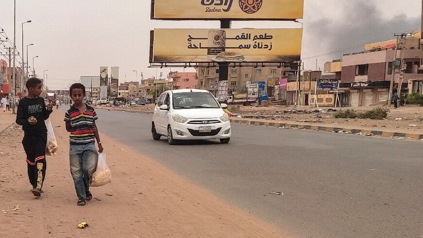 Smoke rises from nearby fighting as children take bags of bread home in Omdurman