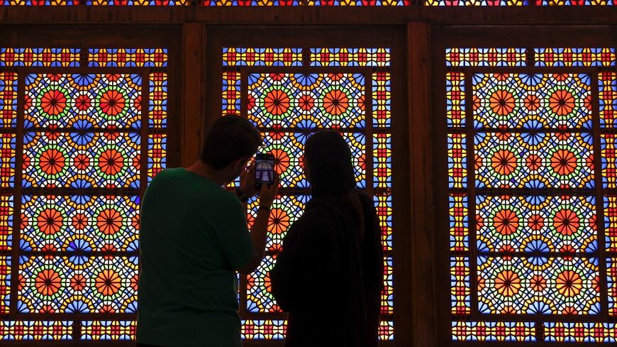 A man and a woman stand in front a stained glass window at Dowlat Abad Garden in Iran's central city of Yazd on July 3, 2023