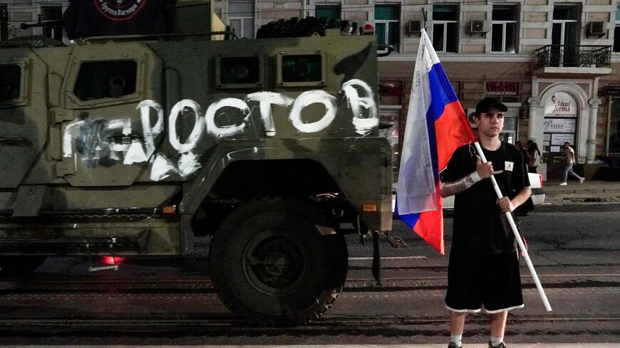 A man holds the Russian national flag in front of a Wagner group military vehicle with the sign read as "Rostov" in Rostov-on-Don late on June 24, 2023. Rebel mercenary leader Yevgeny Prigozhin who sent his fighters to topple the military leaders in Moscow will leave for Belarus and a criminal case against him will be dropped as part of a deal to avoid "bloodshed," the Kremlin said on June 24. (Photo by STRINGER / AFP) (Photo by STRINGER/AFP via Getty Images)