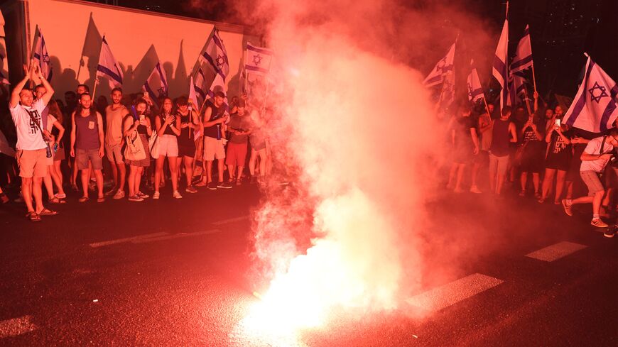 Demonstrators gather around a burning flare during a protest rally against the Israeli government's judicial reform plan in Tel Aviv on July 24, 2023. Israeli lawmakers on July 24 approved a key clause of a controversial judicial reform plan that aims to curb the powers of the Supreme Court in striking down government decisions. (Photo by JACK GUEZ / AFP) (Photo by JACK GUEZ/AFP via Getty Images)