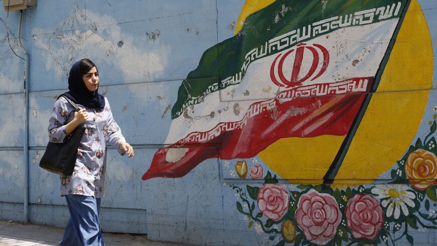 A woman walks in front of a mural painting depicting the Iranian flag, in the capital Tehran on August 6, 2018.