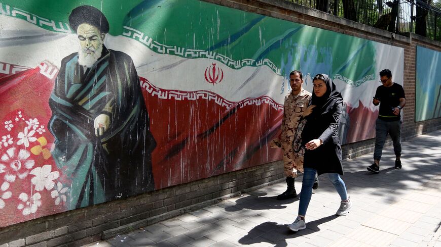 People walk past a mural painting showing the founder of the Islamic republic Ayatollah Ruhollah Khomeini and the national flag along the wall of the former US embassy in the Iranian capital Tehran on June 22, 2019. 