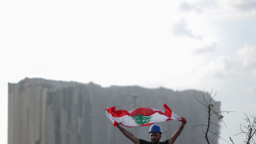 A Lebanese man lifts a national flag during a commemoration ceremony for the victims of the Beirut port explosion across from the capital's harbour, on August 11, 2020. (Photo by PATRICK BAZ / AFP) (Photo by PATRICK BAZ/AFP via Getty Images)