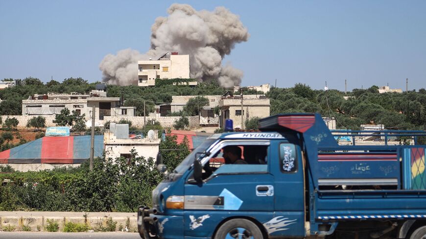 A truck drives on a road as a plume of smoke rises from a building during a reported Russian airstrike on Syria.