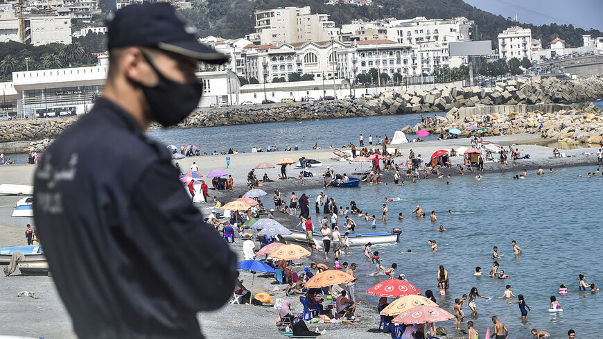 A policeman watches as people cool off in the water at el-Kettani beach in the Bab el-Oued suburb, Algiers, Algeria, Aug. 15, 2020.