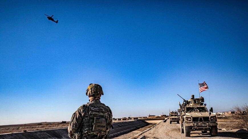 A US AH-64 Apache attack helicopter flies above US soldiers patrolling along the frontlines.