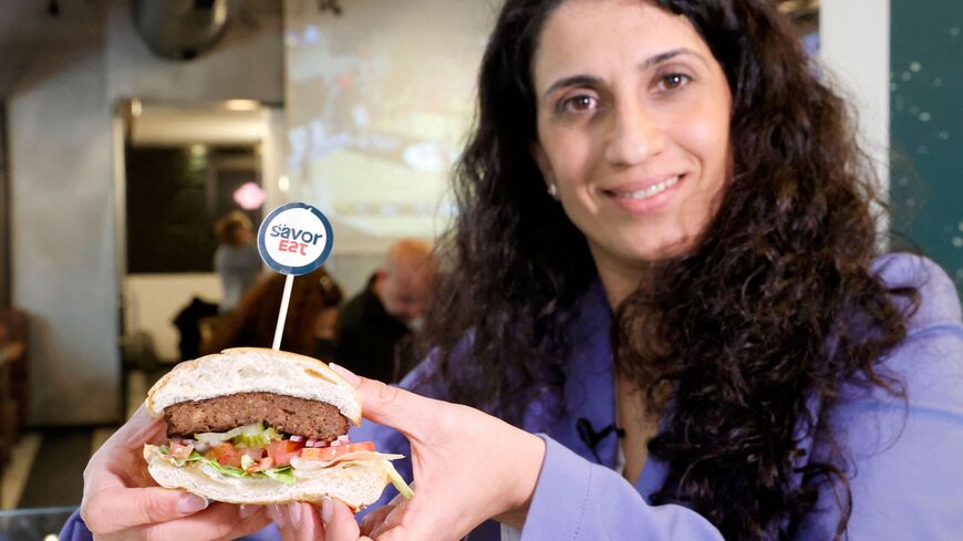 Racheli Vizman, CEO of SavorEat, the start-up specializing in the production of alternatives to meat, holds a cut half of a plant-based patty with a meaty taste, made and cooked by a robot according to customer requirements, offered by Israeli fast food brand BBB in the Israeli coastal town of Herzliya on December 28, 2021. - The Israeli fast food restaurant BBB is serving up a veggie steak made and cooked by a robot that tailors ingredients and cooking time to customer tastes. Customers can use an app to c