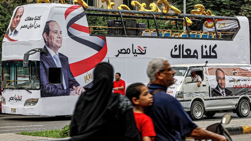 A man, child, and woman ride a motorcycle across the street from an election campaign bus for Egypt's President Abdel Fattah al-Sisi adorned with his image and slogan "Long Live Egypt"