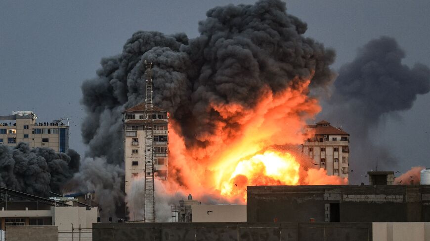 People standing on a rooftop watch as a ball of fire and smoke rises above a building in Gaza City on October 7, 2023 during an Israeli air strike that hit the Palestine Tower building. At least 70 people were reported killed in Israel, while Gaza authorities released a death toll of 198 in the bloodiest escalation in the wider conflict since May 2021, with hundreds more wounded on both sides. (Photo by MAHMUD HAMS / AFP) (Photo by MAHMUD HAMS/AFP via Getty Images)
