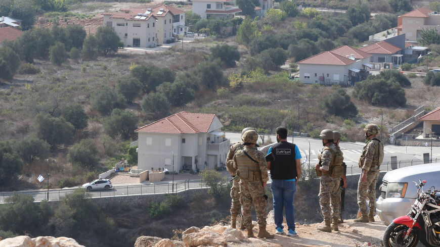 Lebanese soldiers and bystanders stand on a road overlooking the border area with the northern Israeli town of Metulla (background), Oct. 9, 2023.