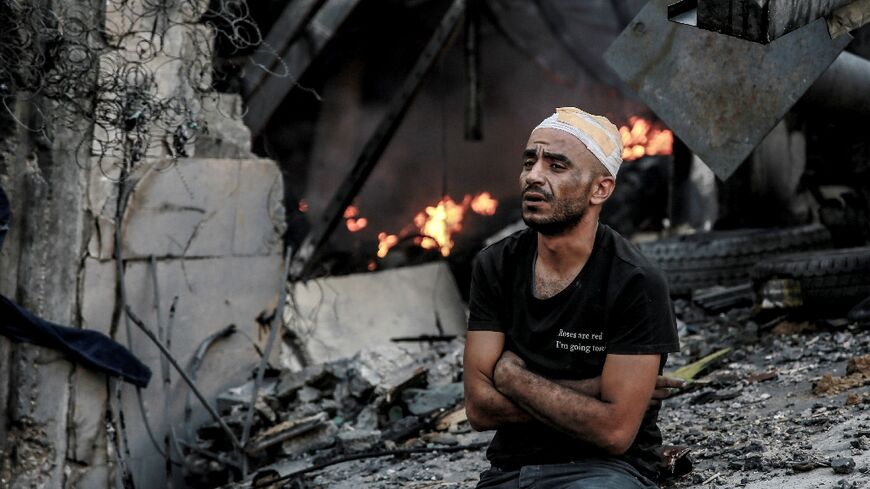 An injured man sits in front of a smouldering building in the aftermath of an Israeli strike on Gaza City on Thursday