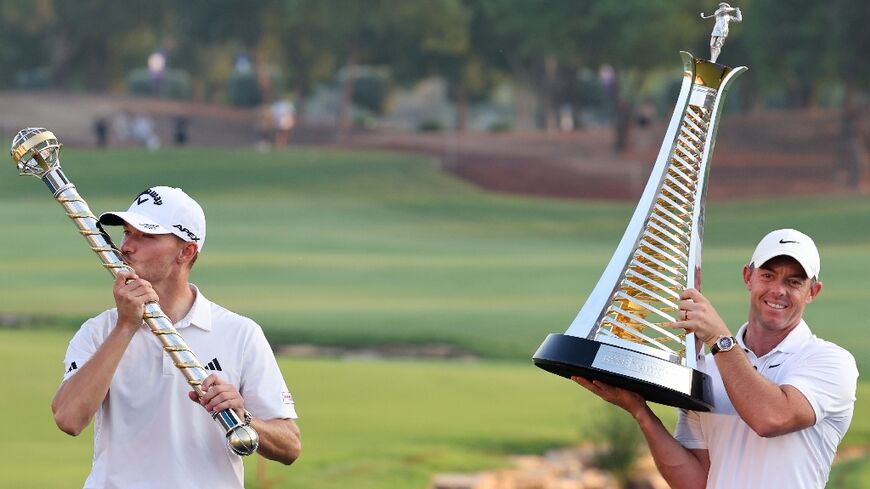 Nicolai Hojgaard (L) kisses the winner's trophy as Rory Mcllroy (R) lifts the world championship trophy after the last day of the DP World Tour Championship 