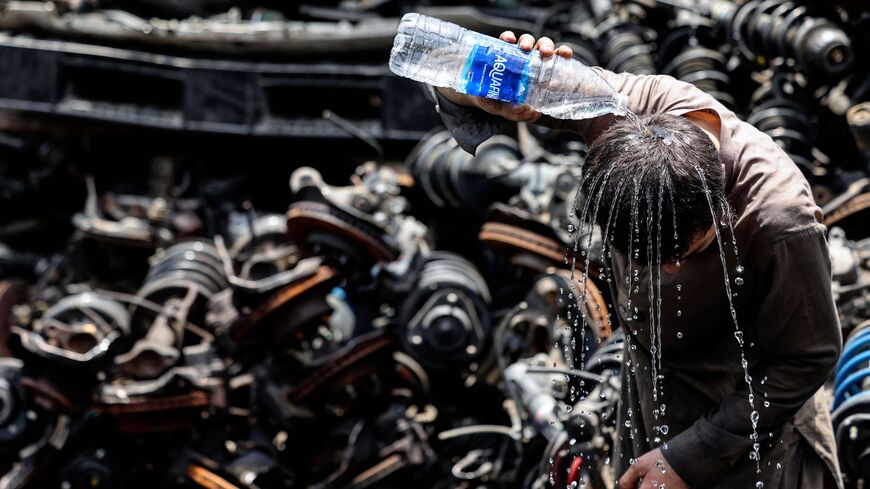 A foreign laborer pours water on his head as he tries to cool off during his working day.