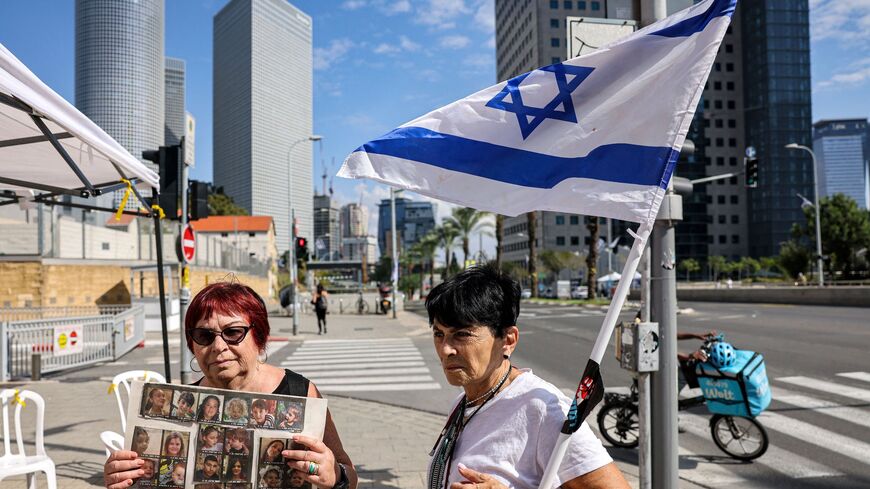 An elderly woman stands with an Israeli flag next to another holding a sign showing the faces of young Israeli hostages held by Palestinian militants since the October 7 attack near Azrieli Mall in Tel Aviv on October 18, 2023. (Photo by AHMAD GHARABLI / AFP) (Photo by AHMAD GHARABLI/AFP via Getty Images)